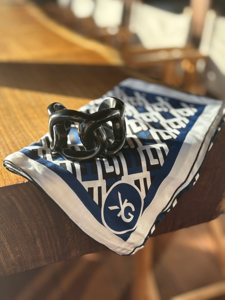 Black cat-shaped object on a blue and white patterned cloth with a logo on a wooden surface.